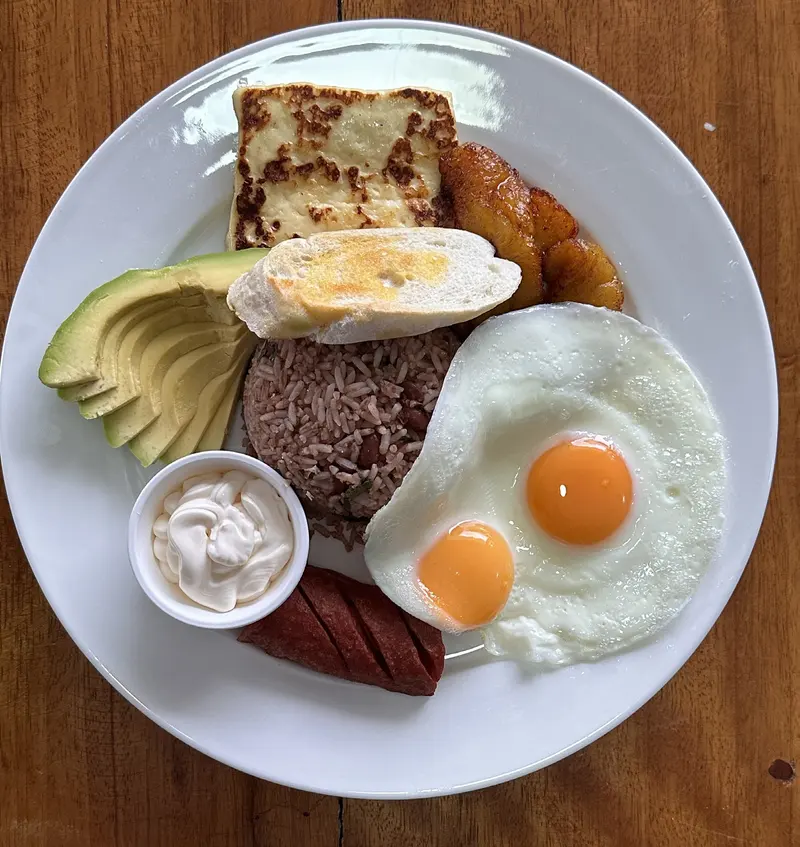 Desayuno típico con gallo pinto, dos huevos fritos, queso frito, plátano maduro, aguacate, natilla y salchichón