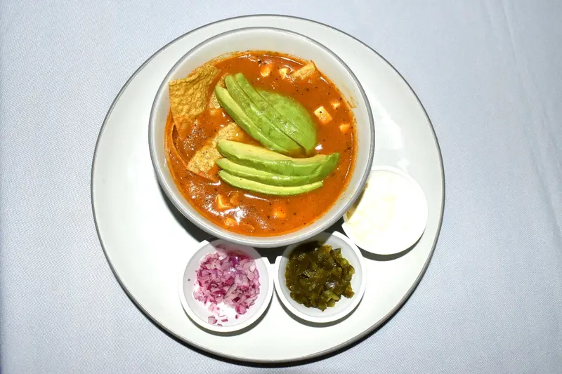 Sopa de tomate con aguacate, tortilla tostada y guarniciones